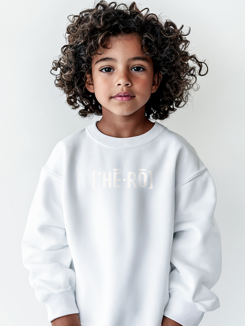 A child with curly hair wearing a white sweatshirt featuring the text HERO in bold letters. The relaxed fit and soft fabric highlight both comfort and a bold statement.