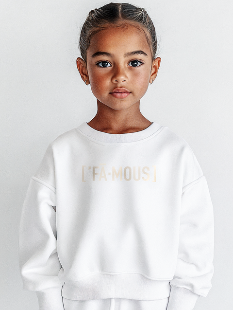 A young girl in a crisp white sweatshirt with the text FAMOUS subtly printed on the chest. The clean design creates an elegant yet youthful aesthetic.