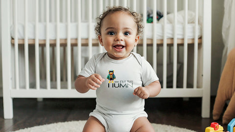 Smiling baby sitting on the floor in front of a crib, wearing a white ['LIT·TLE] HŪMN onesie with a bear graphic. The baby is happy and playful, with toys nearby, in a cozy, modern nursery setting that reflects a stylish and youthful vibe.