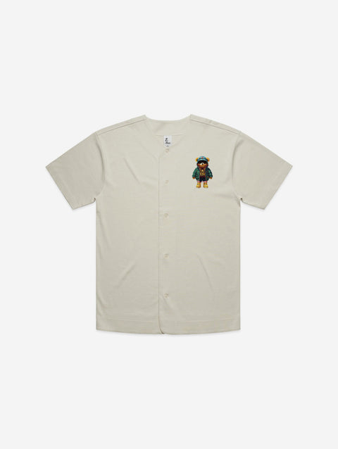 A bone-colored baseball jersey featuring a vibrant, embroidered bear patch on the chest, combining sporty style with a playful and unique detail.