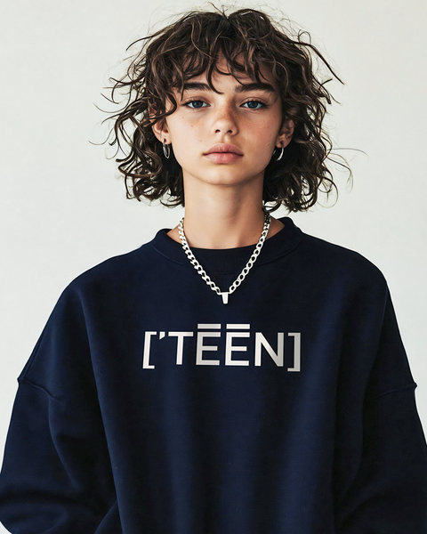 A stylish teen girl with curly hair wearing a navy sweatshirt featuring TEEN in sleek metallic print. The outfit is accessorized with a silver chain necklace, emphasizing a mix of casual and edgy style.