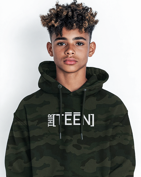 A teenage boy with short curly hair wearing a green camouflage hoodie with the text THIRTEEN printed in clean white. The look is bold yet approachable, capturing a sporty and adventurous vibe.