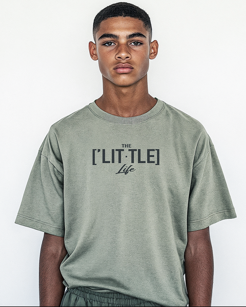 A teenage boy standing in a sage green oversized t-shirt with THE LITTLE Life printed in a simple yet striking design. The look reflects comfort and a laid-back modern aesthetic.